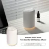 White wireless waterless essential oil diffuser with ambient warm light and an oil bottle placed on a modern desk