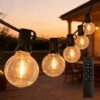 G40 Outdoor String Lights Sunset Patio Lifestyle Warm glowing G40 LED string lights hanging on an outdoor patio deck at sunset with a wireless remote control